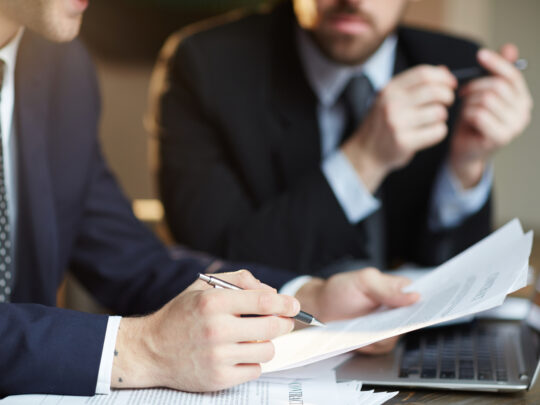 Closeup portrait of two unrecognizable  business partners reviewing paperwork and signing contract papers at table during meeting